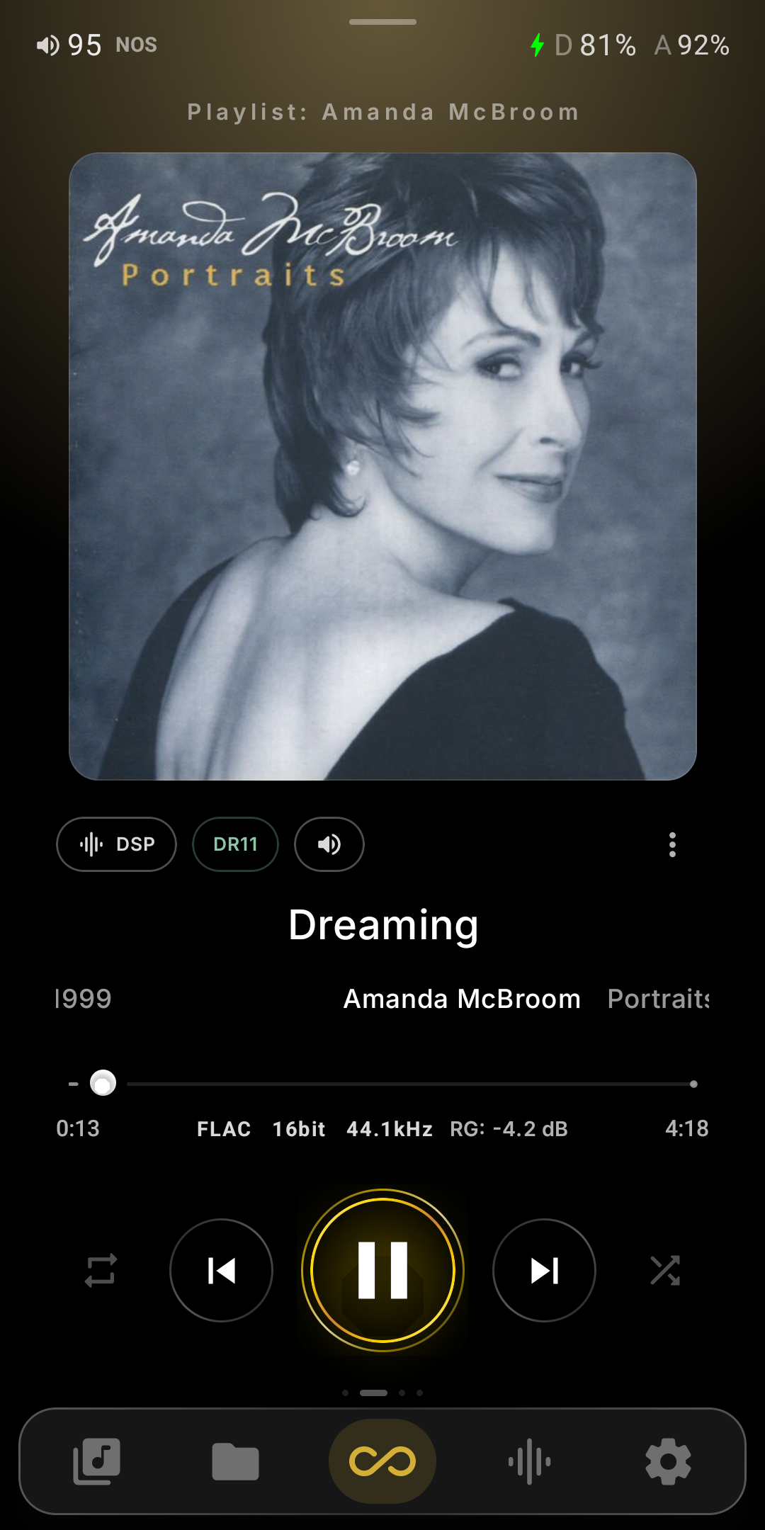 The redesigned Now Playing screen in Infinity Player V10.5 — volume and NOS state plus dual D and A battery readouts along the top, the playlist name, large album art on an ambient glow, a DSP / DR11 / volume chip row, track title with year, artist and album, a seek bar with FLAC 16bit 44.1kHz and ReplayGain inline, gold-ringed transport controls, page dots, and the persistent bottom navigation bar.